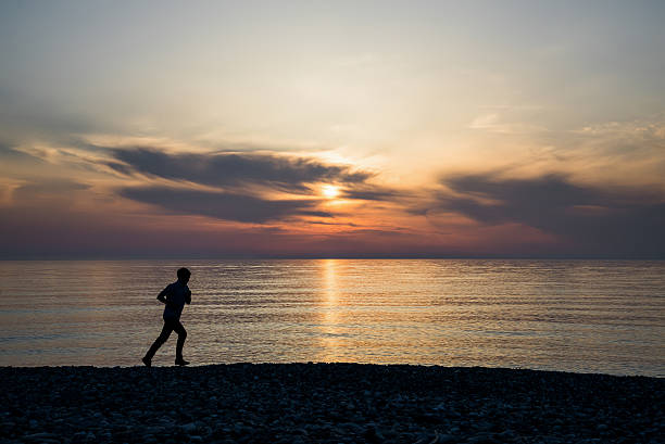 Backlight of a man running on the beach at sunset with the horizon in the background.