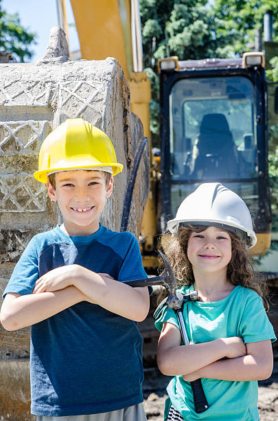 istock Two kids, wearing hardhat, in front of construction caterpillar 542203602