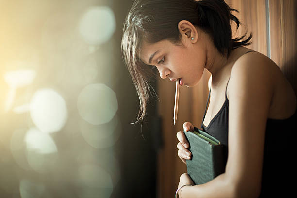 girl looking down and thinking while holding book and pencil. - spaghettibandjes stockfoto's en -beelden