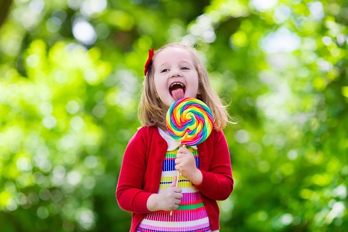 Cute little girl with big colorful lollipop. Child eating sweet candy bar. Sweets for young kids. Summer outdoor fun. Preschooler kid with sugar lolly. Children having snack in a park after preschool.
