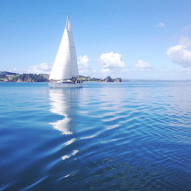Plain sailing A sailboat on a calm blue sea with ripples and reflections. Filtered image with grain. Photographed in the Bay of Islands, New Zealand. bay of islands new zealand stock pictures, royalty-free photos & images