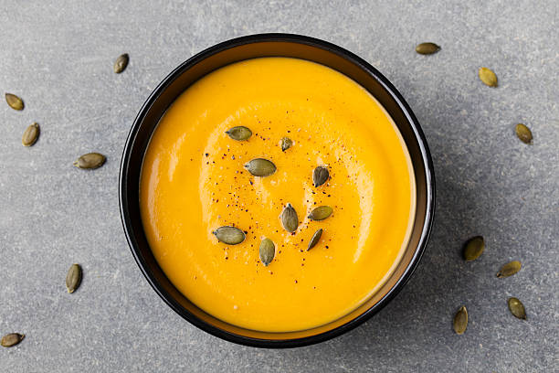 Pumpkin cream soup with pumpkin seeds in a black bowl Pumpkin cream soup with pumpkin seeds in a black bowl. Grey stone background. Top view. pumpkin soup photos stock pictures, royalty-free photos & images