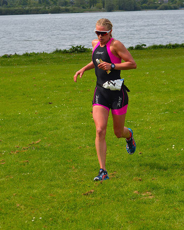 Grafham, Cambridgeshire, England - May 22, 2016:  Female triathlete on running stage of triathlon, wearing race suit.