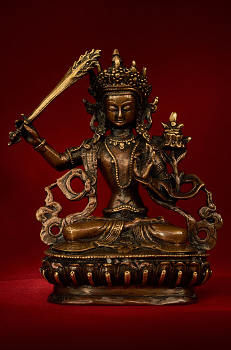 Statuette of Manjushri brandishing sword of wisdom on a red background. Manjushri, Still a Youth. Vajrayana deity.