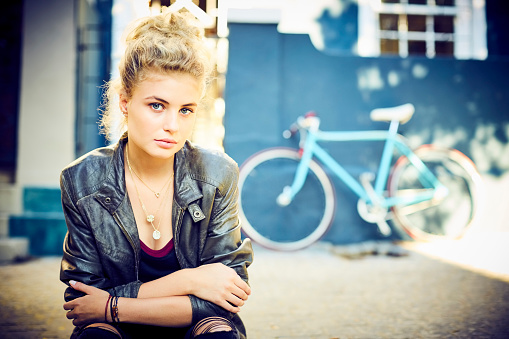 Portrait of fashionable young woman sitting on sidewalk. Confident female is with arms crossed. She is wearing casuals.