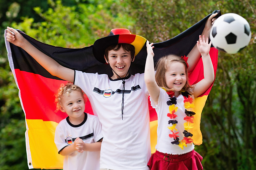 Children cheering and supporting German national football team. Kids fans and supporters of Germany during soccer championship. Family with teenager boy, little girl and baby watch football game.