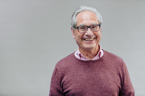 Portrait of a natural smiling, happy senior French businessman with glasses and smart casual, real people studio shot with copy space on gray background. XXXL