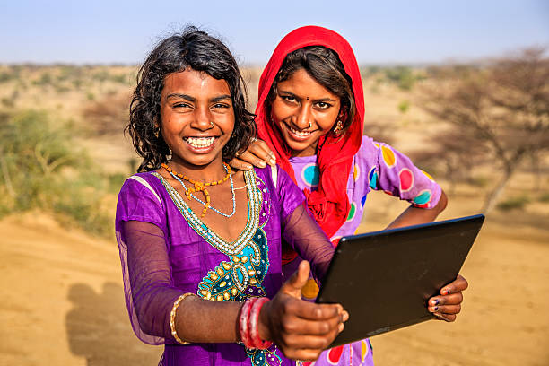istock Happy Indian young girls using digital tablet, desert village, India 542312062
