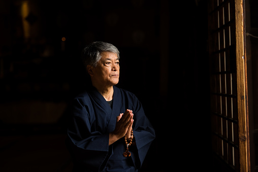 Senior aged Japanese man praying with beads at a Japanese temple