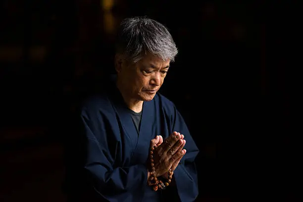 Senior aged Japanese man praying with beads at a Japanese temple