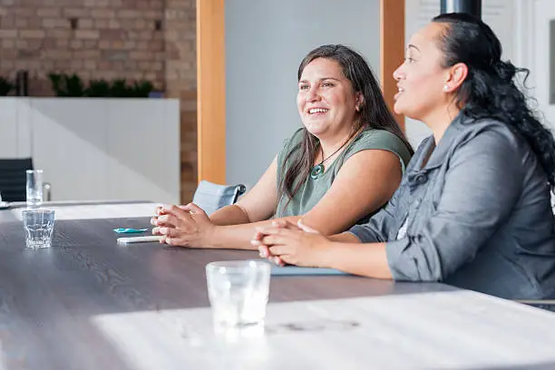 Two Maori women on one side of table in involved in discussion during business meeting