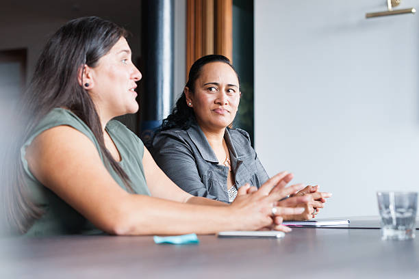 Two Maori women at table in business meeting Two Maori women on one side of table in involved in discussion during business meeting pacific islander ethnicity stock pictures, royalty-free photos & images