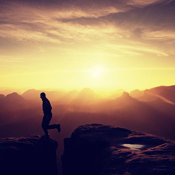 istock Hiker in black is jumping between mountains peaks. 542322538