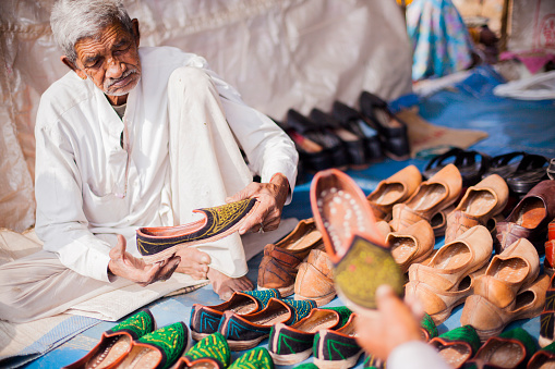 A senior indian adult shoe vendor at his shop at the Pushkar camel fair in Rajsathan, India