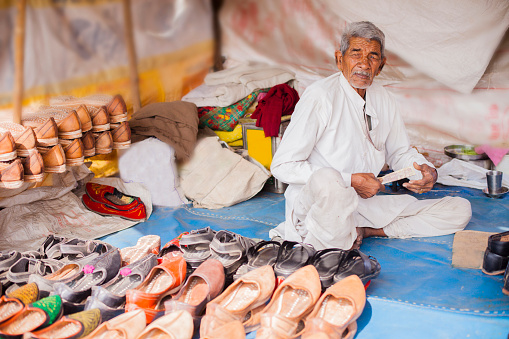 A senior indian adult shoe vendor at his shop at the Pushkar camel fair in Rajsathan, India