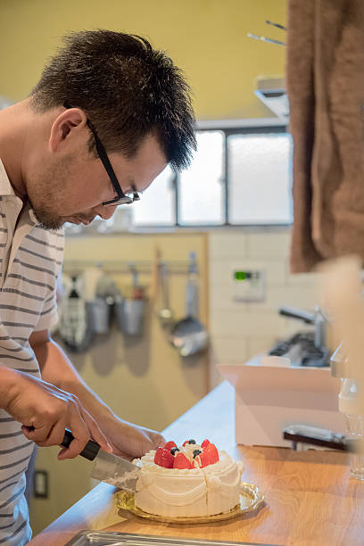 istock Japanese Man Cutting Birthday Cake with Knife in Home Kitchen 542562372