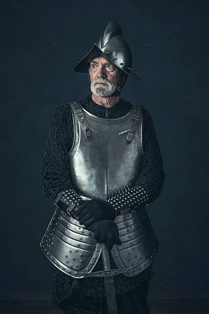 istock Bearded knight standing with sword in front of gray wall. 542564634