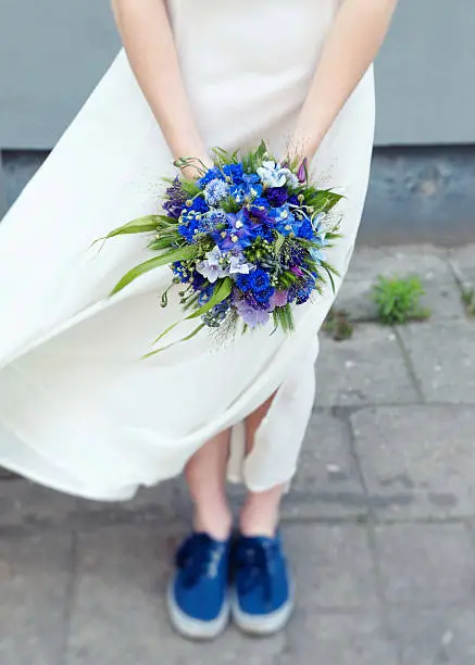 Photo of Young, hip bride holding bouquet of wildflowers matching her sneakers.