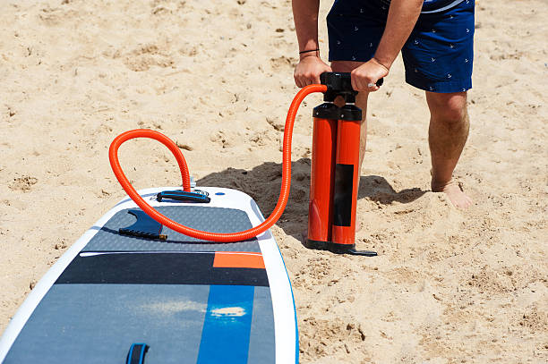 SUP Stand up paddle board pump man inflates a rubber board on the beach SUP sand river stock pictures, royalty-free photos & images