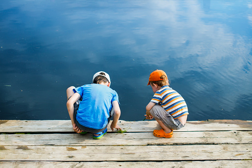 two boys looking into the water from the wooden pier. view from the back. safety concept