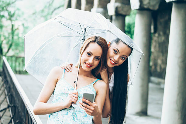 amis se cachent sous un parapluie sous la pluie - rain women umbrella parasol photos et images de collection