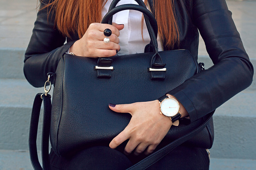 Trendy young girl in black leather jacket holding big black handbag street background .  Fashion accessories