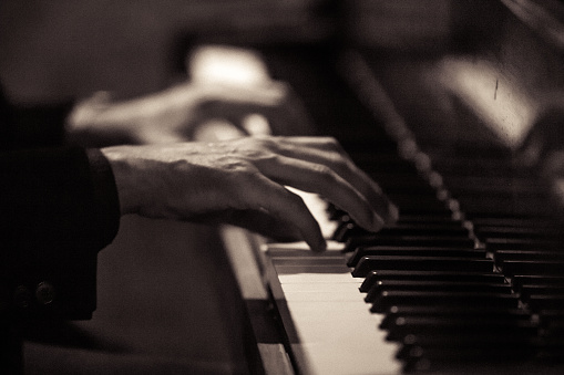 Black and white close up shot of an unrecognizable man playing the piano.