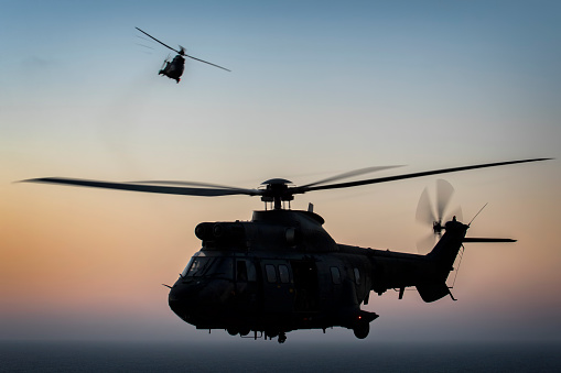 Silhouette aerial view of Army helicopters flying over mountains at sunset. 