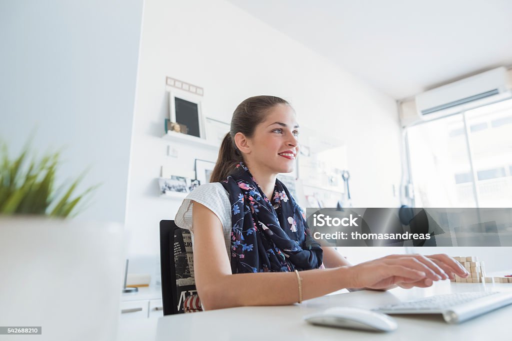 Woman professional is typing, using a keyboard Beautiful woman creative professional is smiling, seating on her desk, typing on a keyboard, while in a modern working environment Ergonomics Stock Photo