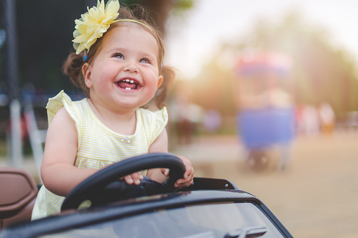 little one year old baby girl sitting in electric toy car , and having fun , enjoying and smiling  , showing her teeth
