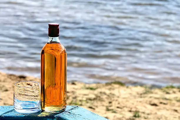 Bottle of whiskey and tumbler on the shore of lake