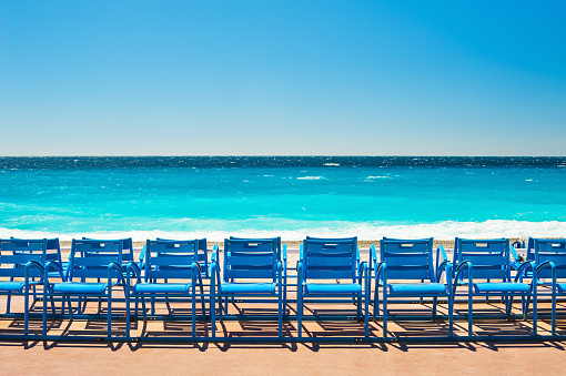 Side view of elegant blonde woman with sun hat looking at blue-white parasols on French Riviera sea beach. Copy space