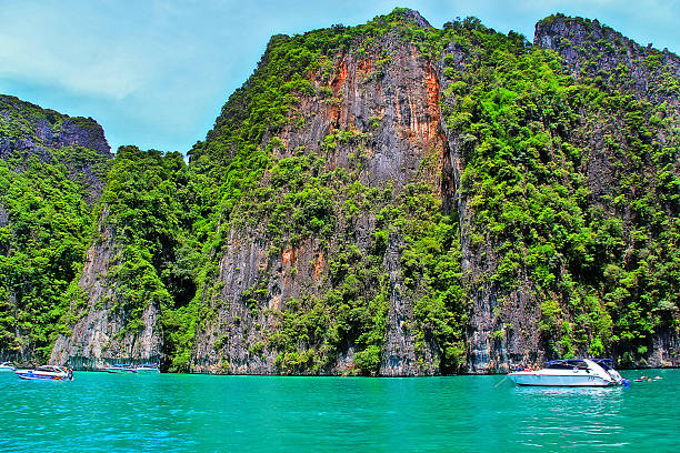 Krabi, Thailand - May 28, 2013 - Tourist sightseeing boats with rock mountain at Maya beach in Andaman sea.