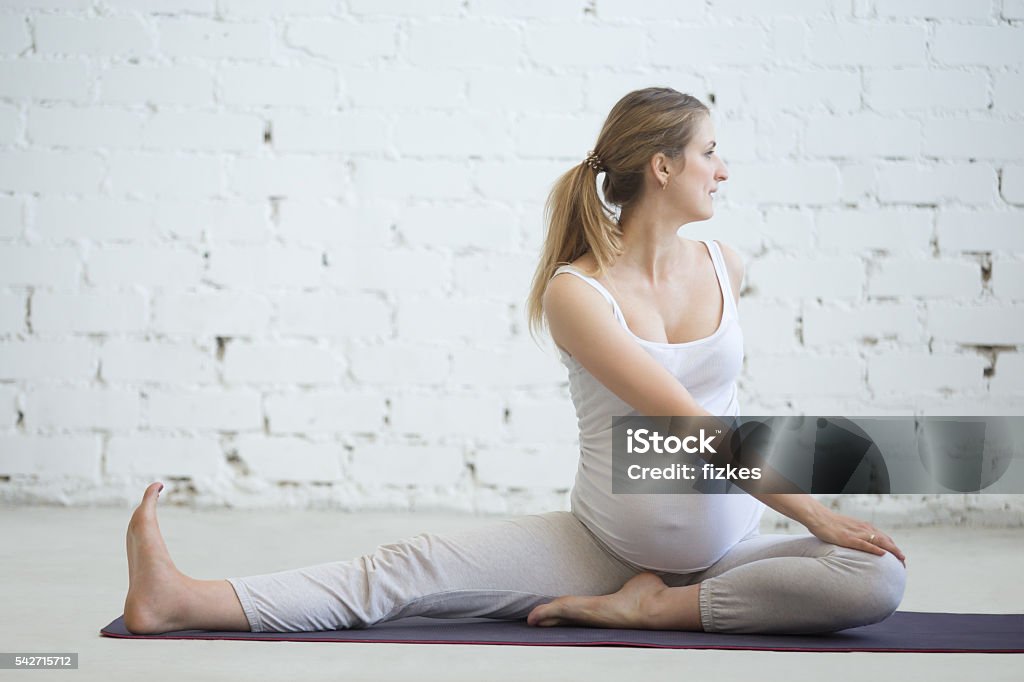 Pregnant young woman doing prenatal yoga. Spinal twist Pregnancy Yoga and Fitness concept. Portrait of young pregnant yoga model working out indoors. Pregnant fitness person practicing yoga at home. Prenatal gentle spinal twist in Janu Sirsasana pose Activity Stock Photo