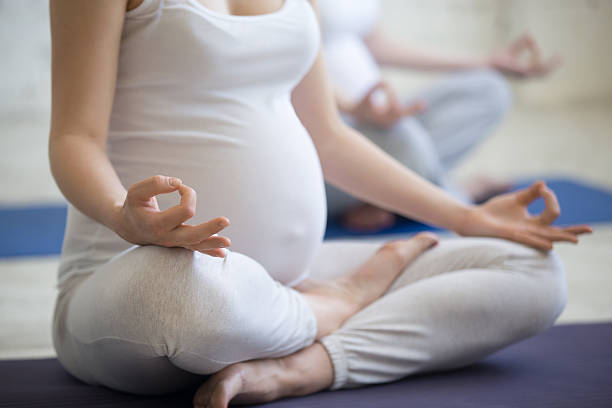 Pregnant young women doing prenatal yoga. Close-up of torso Pregnancy Yoga, Fitness concept. Torso close-up of two beautiful young pregnant yoga models working out indoors. Pregnant fitness women sitting in yogic cross-legged pose at class. Prenatal meditation sukhasana stock pictures, royalty-free photos & images