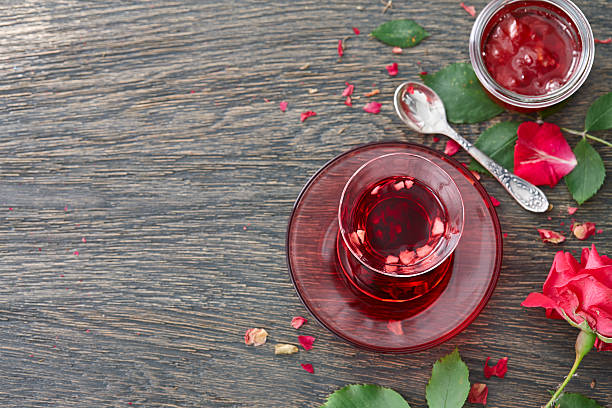 Hibiscus tea with rose jam background Food background with a glass turkish cup of hibiscus tea with fruit pieces, rose jam and rose flower on a dark wooden background. pink tea stock pictures, royalty-free photos & images