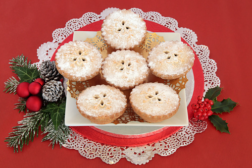 Mince pie christmas cakes with holly and bauble decorations over red background.