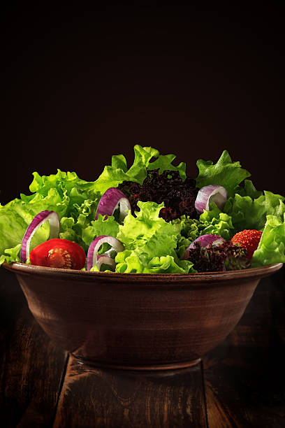 Salad with fresh vegetables and herbs in a clay bowl on a wooden table