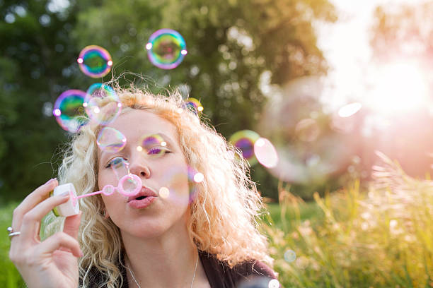 istock Playful woman blowing soap bubbles in nature. 542725466