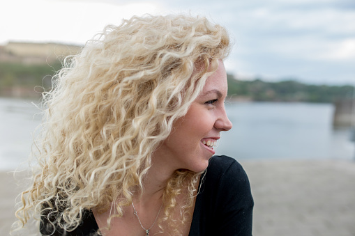 Side view of young woman with curly hair laughing outdoors during a day.