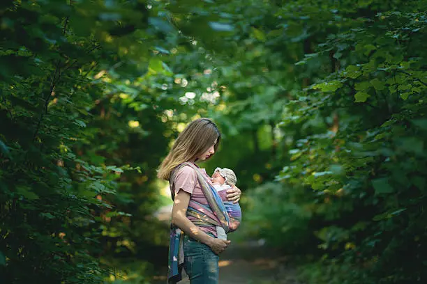 Young Mom carrying her daughter in a sling during their outdoor walk.