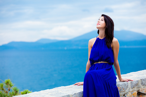 portrait of the beautiful young woman sitting on the stone railing  in Greece