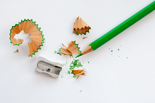 sharpener, green wooden pencil and pencil shavings on white