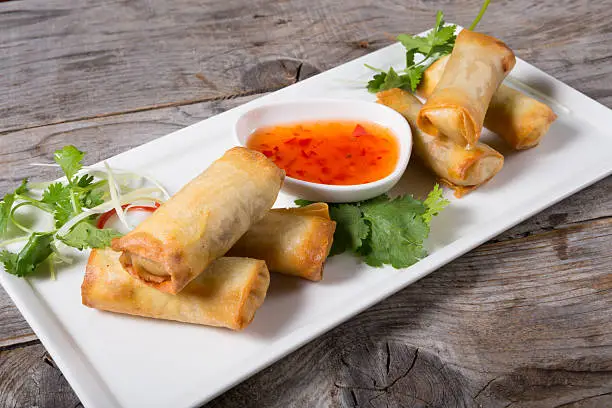Spring rolls with chili sauce on wooden board