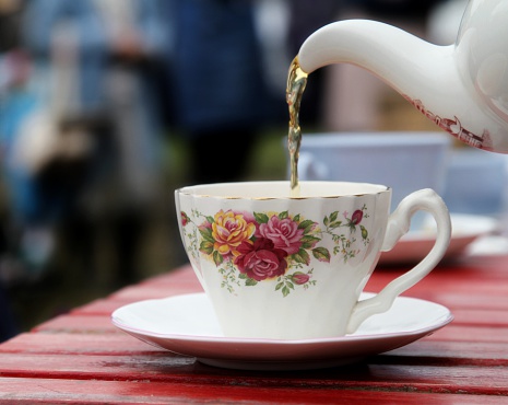 Tea being poured from floral patterned teapot into a bone china cup
