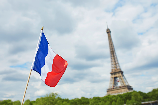 French national flag (tricolour) in Paris with the Eiffel tower in the background. July the 14th, French national holiday concept
