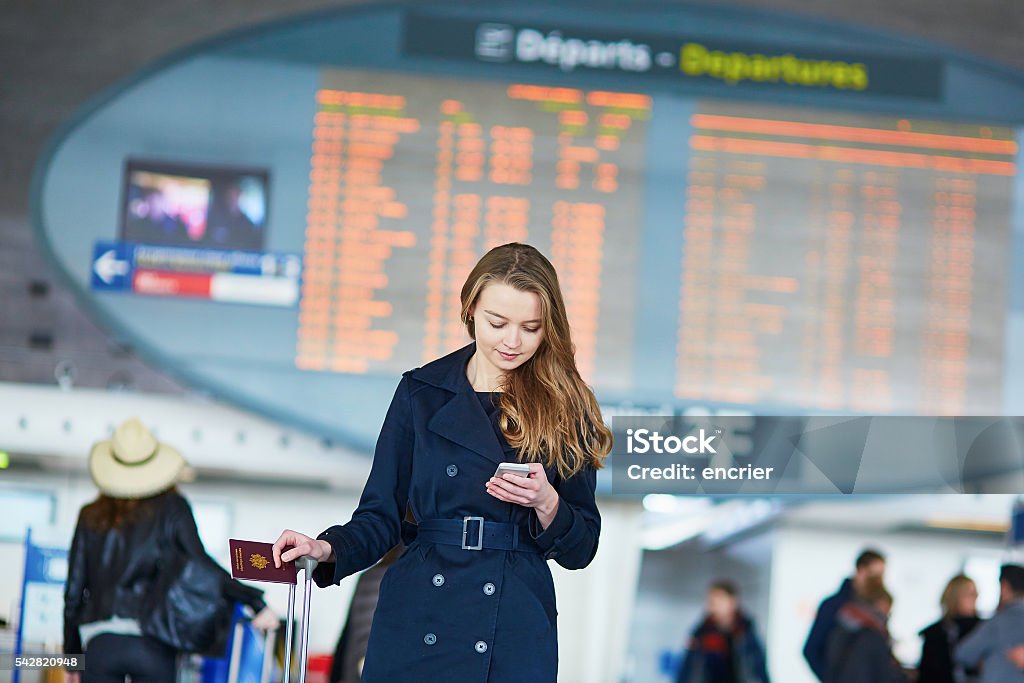 Young female traveler in international airport Young woman in international airport near the flight information board, using her mobile phone Adult Stock Photo