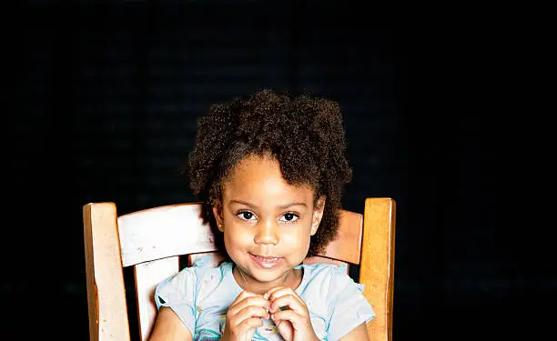 African American young girl/child with natural hair pose sitting playing with her hands looking forward.