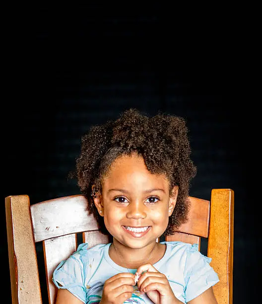 African American young girl/child with natural hair pose sitting with big smile playing with her necklace