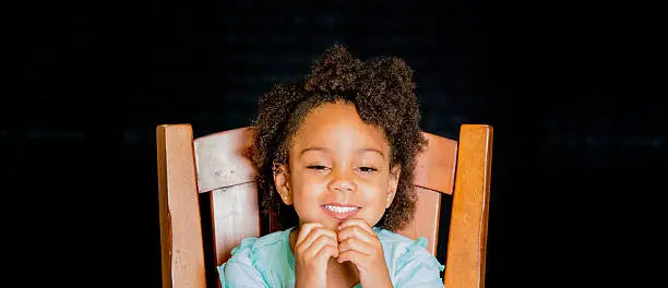 African American young girl/child with natural hair pose sitting squinting eyes smile while playing with her necklace